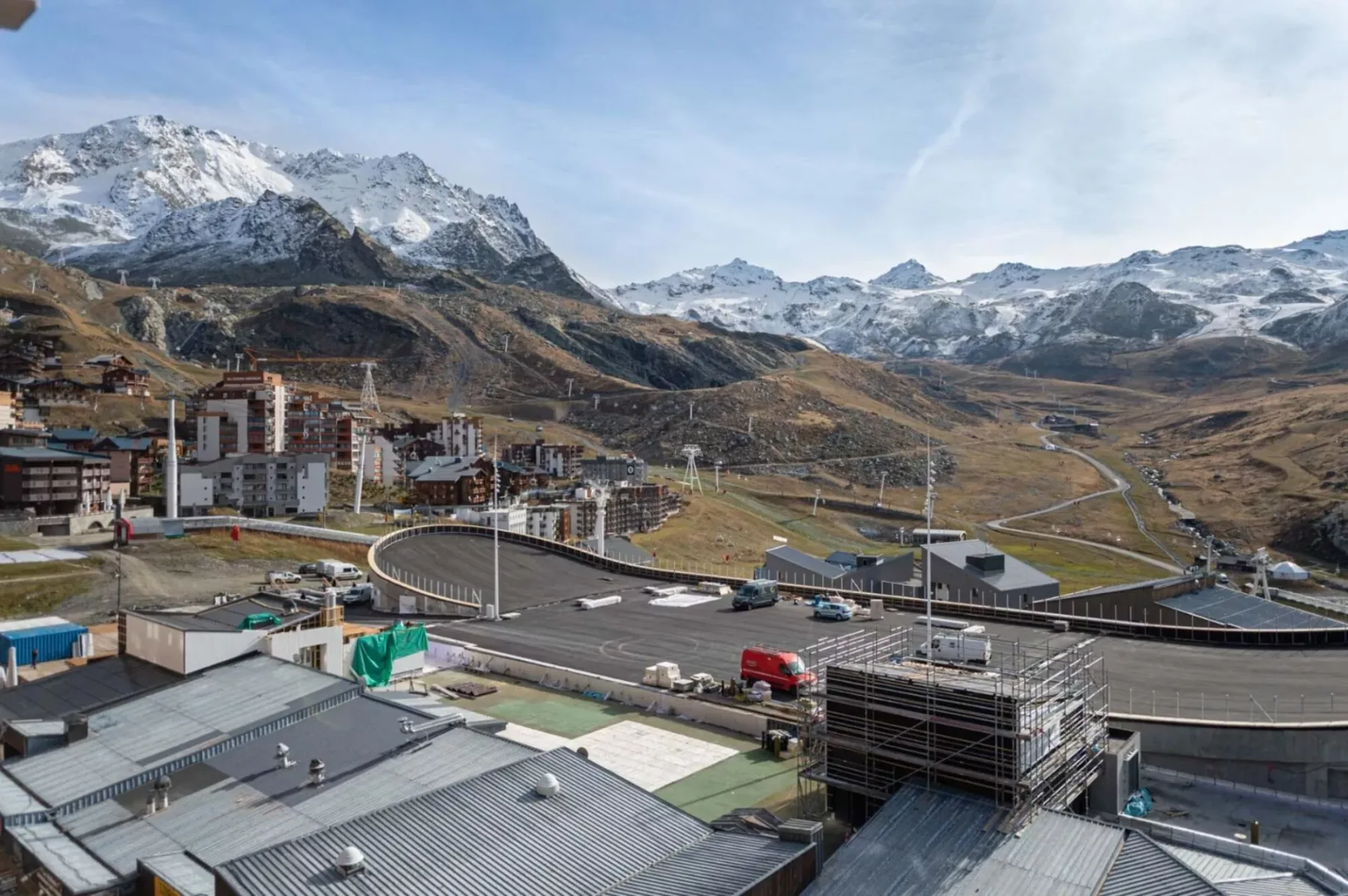 Un valle de montaña con picos nevados, edificios en la ladera y una carretera sinuosa.