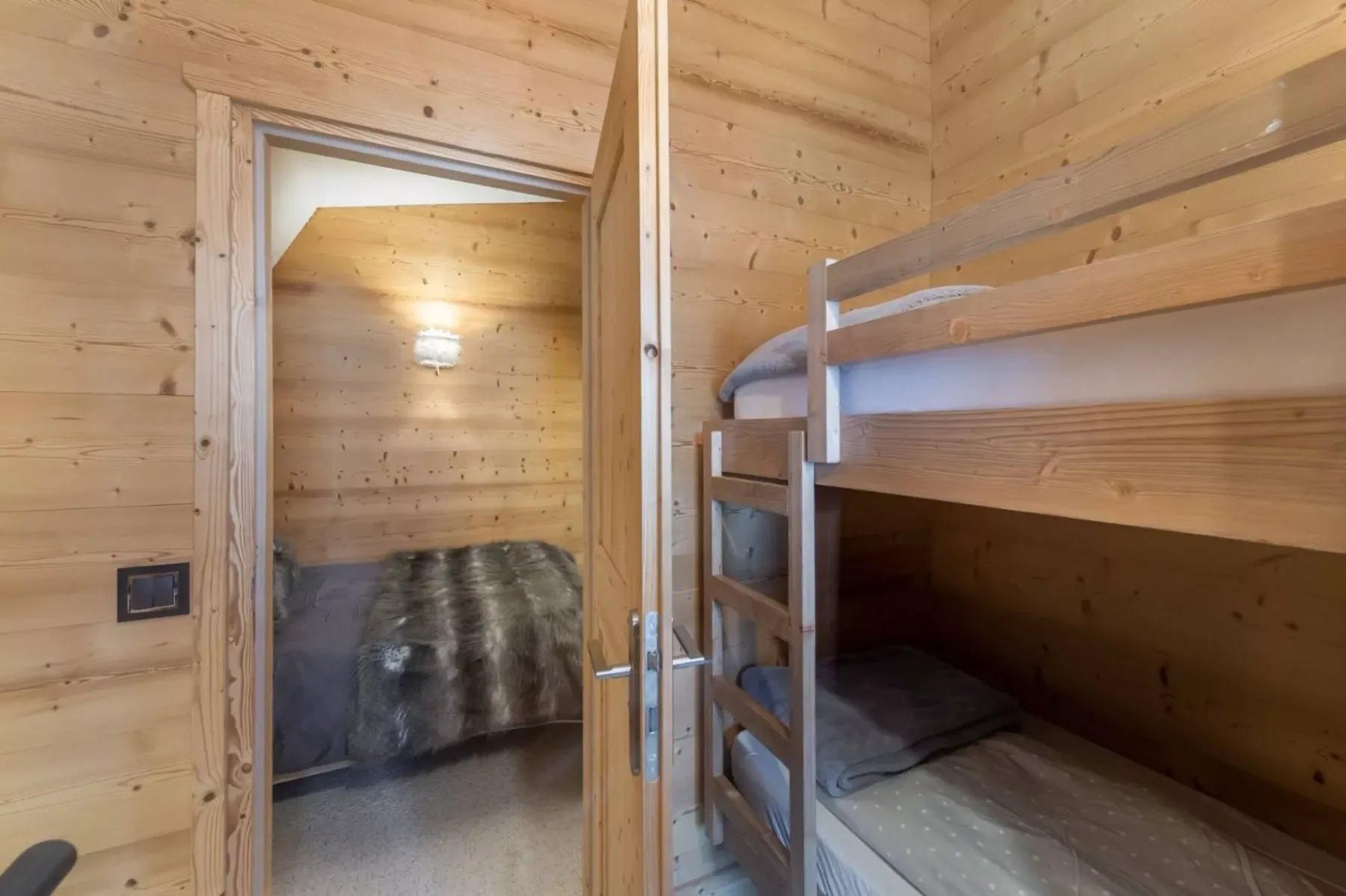 Dormitorio revestido de madera con una litera junto a una puerta abierta.