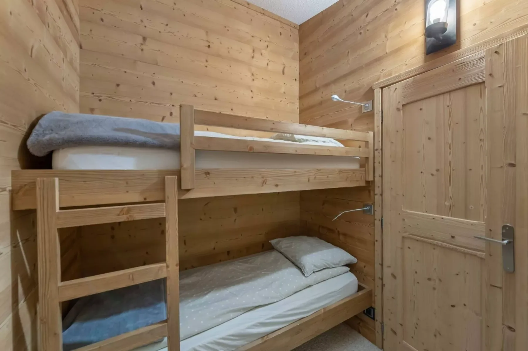 Dormitorio revestido de madera con literas y ropa de cama blanca.