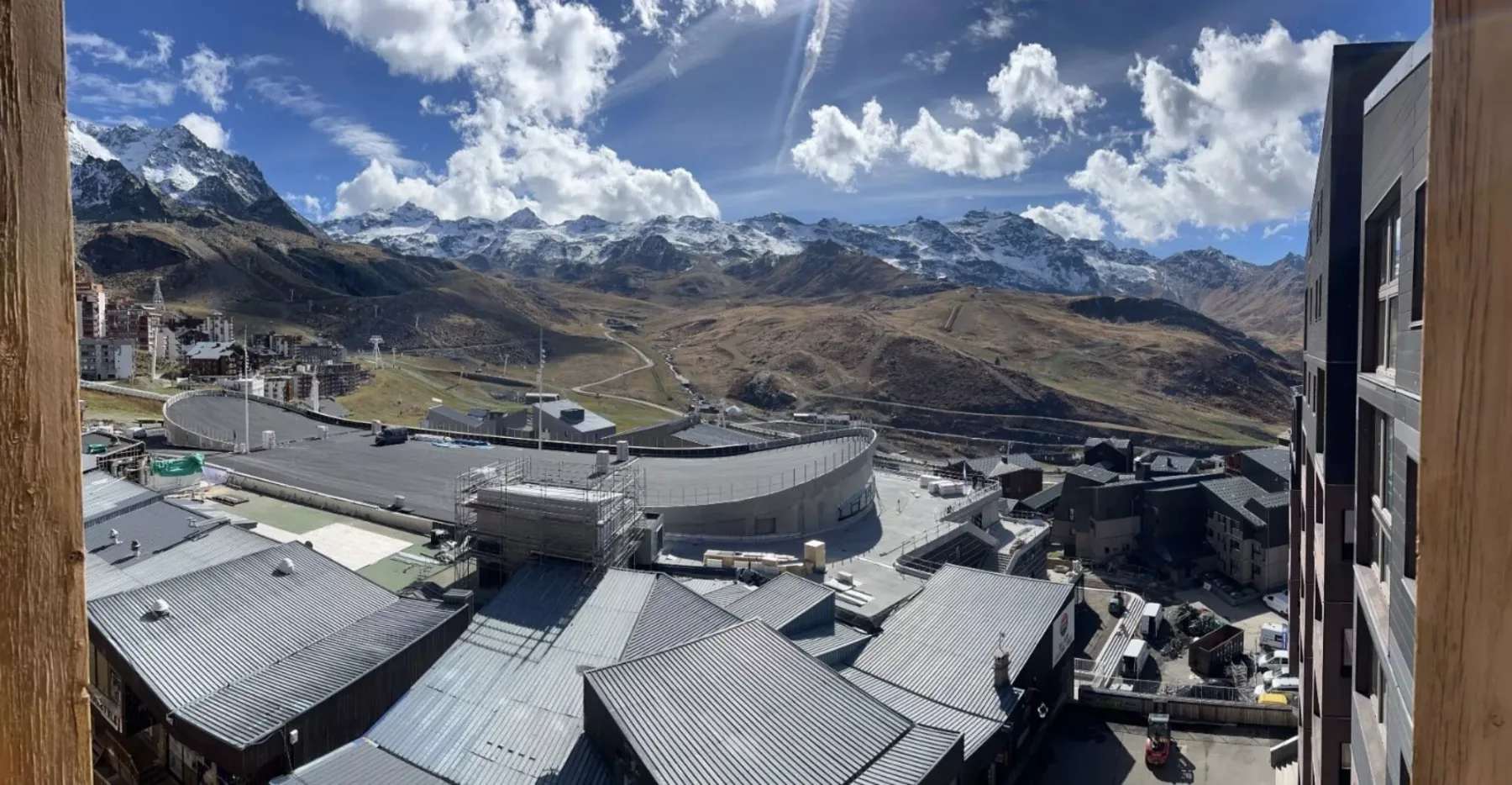 Las montañas se elevan tras un conjunto de tejados bajo un cielo azul con nubes.