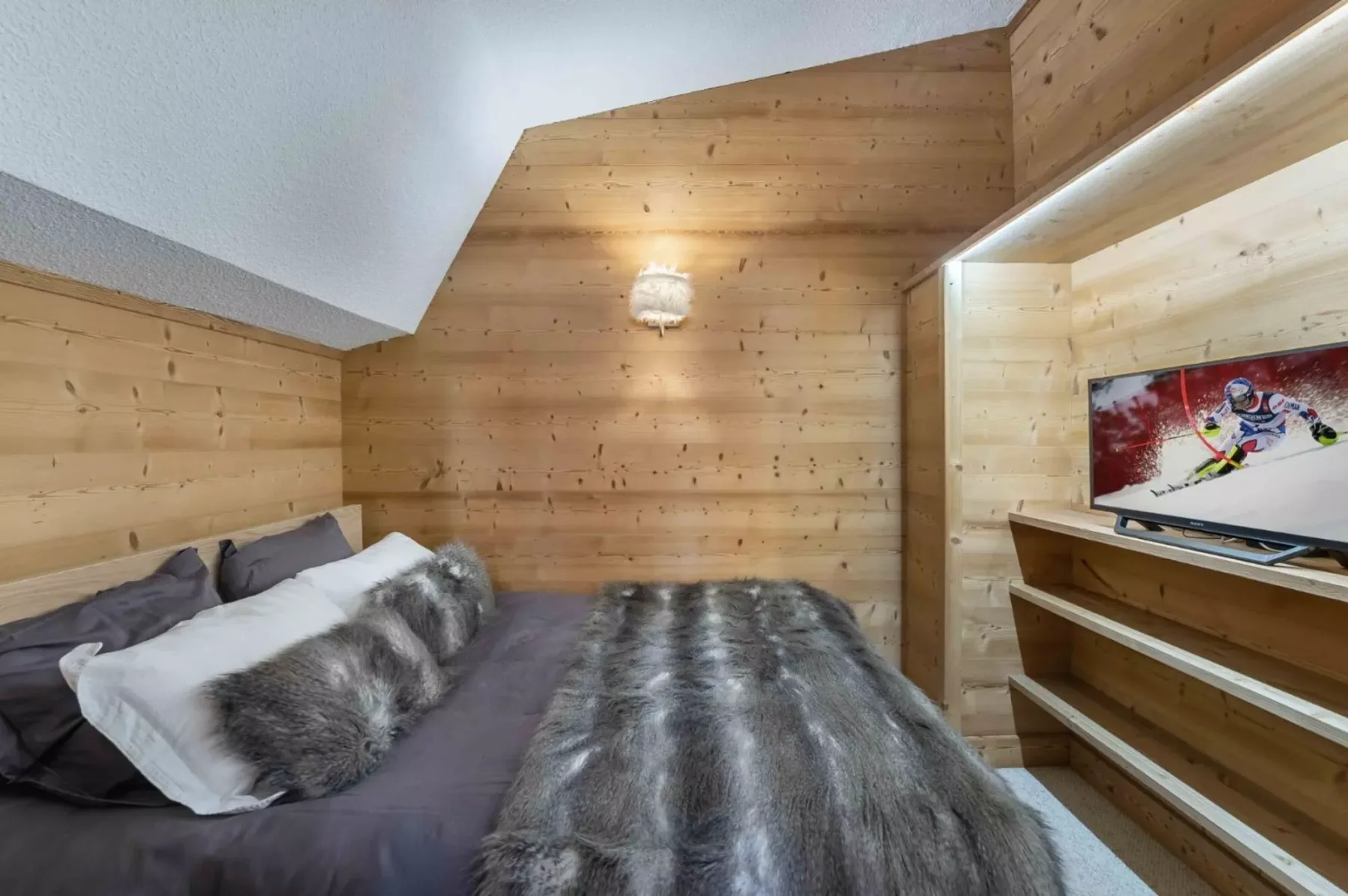 Un dormitorio con una cama cubierta con ropa de cama gris y un televisor en la pared.