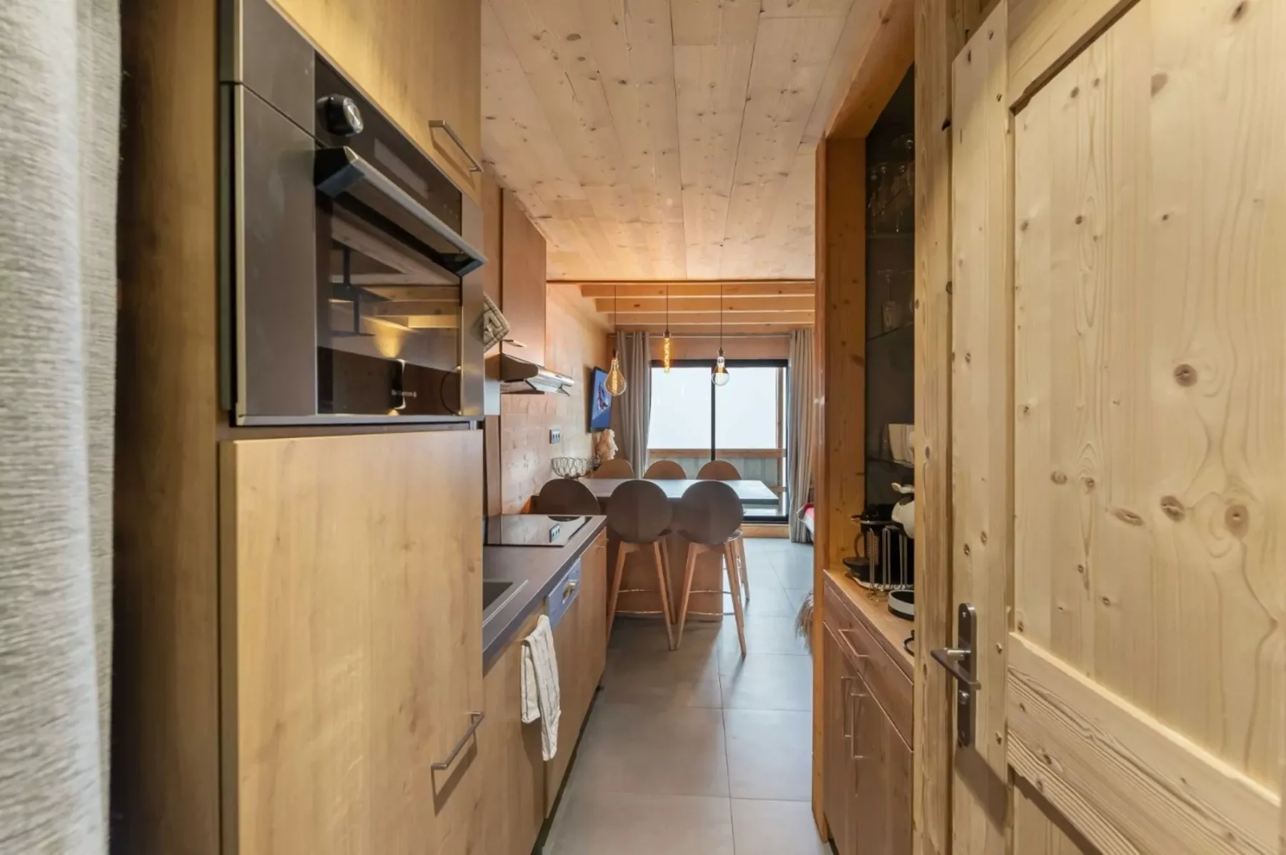 Una cocina estrecha con gabinetes de madera y un comedor al fondo.