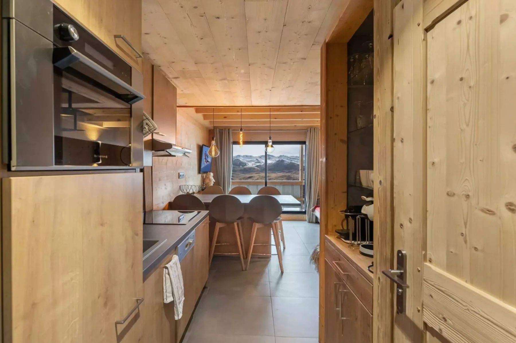 Una cocina compacta con una barra y taburetes, abierta a una vista de montañas.