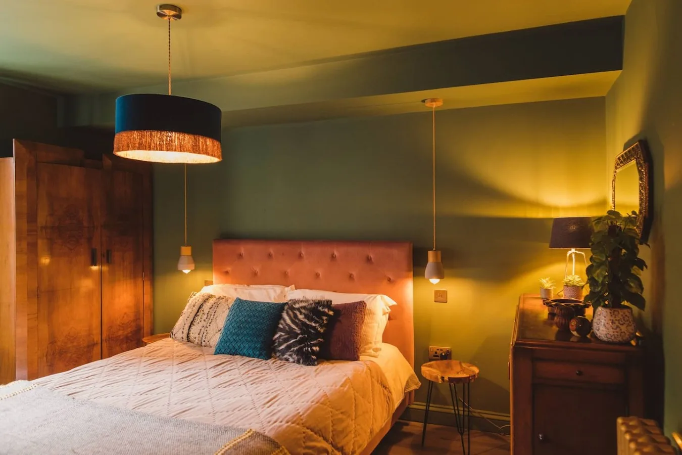 A warmly lit bedroom features a bed with colorful pillows and wooden furnishings.