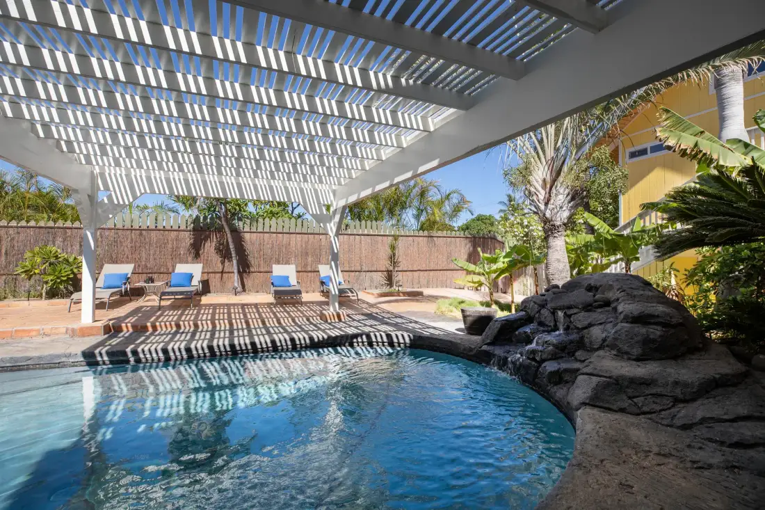 An outdoor swimming pool sits beside a shaded patio with lounge seating.