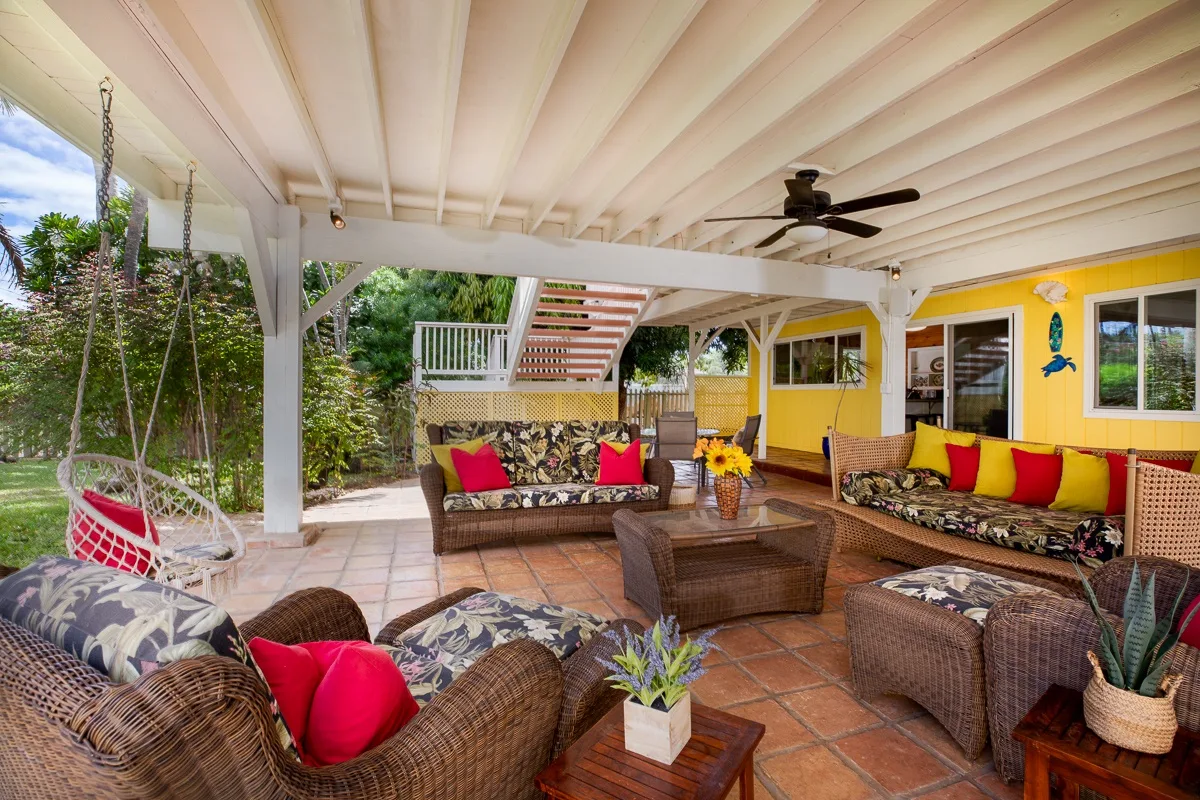 A covered patio seating area with colorful cushions and a ceiling fan.
