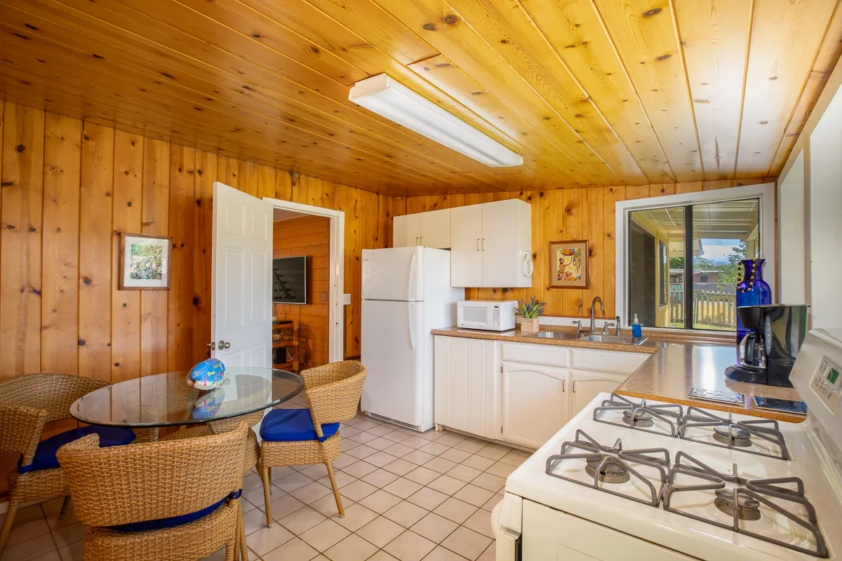 A wood-paneled kitchen with white cabinets, a refrigerator, and a gas stove.