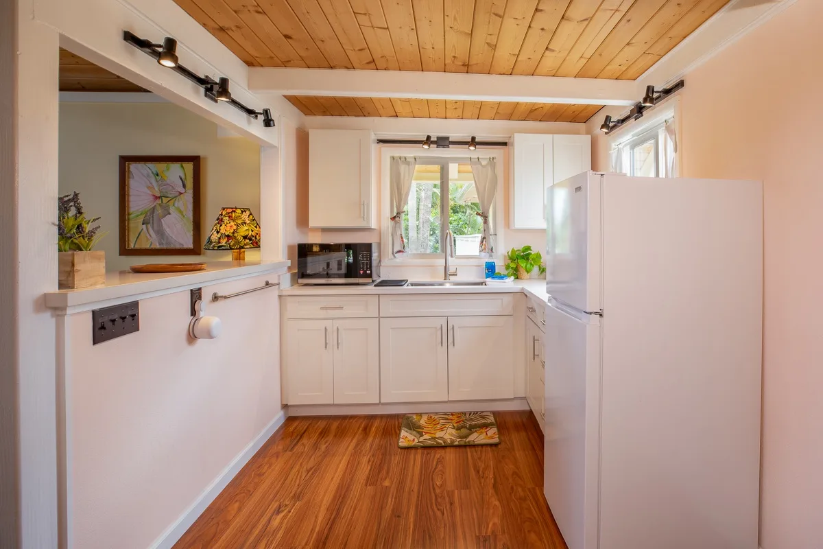 A compact kitchen with white cabinets, a refrigerator, and a window above the sink.