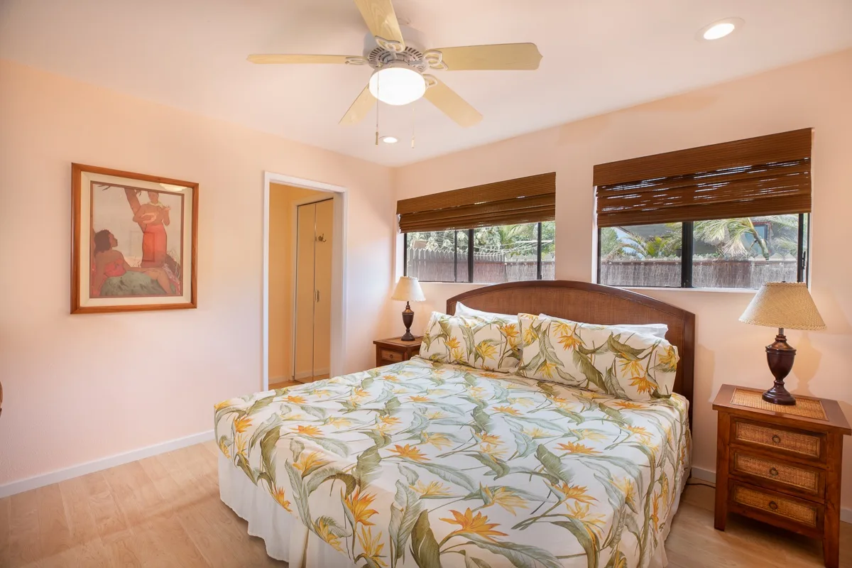 A bedroom with a bed covered in floral bedding and windows with blinds.