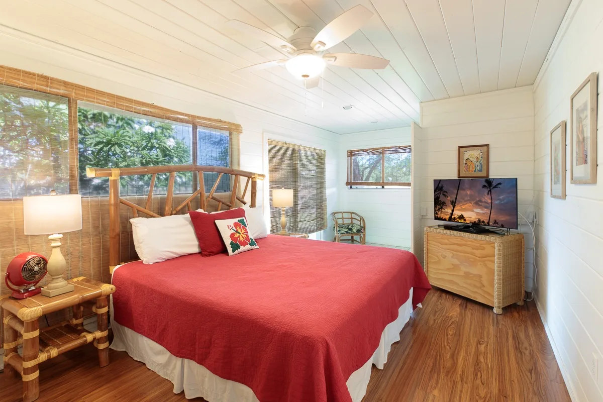 A bedroom with a red-covered bed, wooden furnishings, and a ceiling fan.