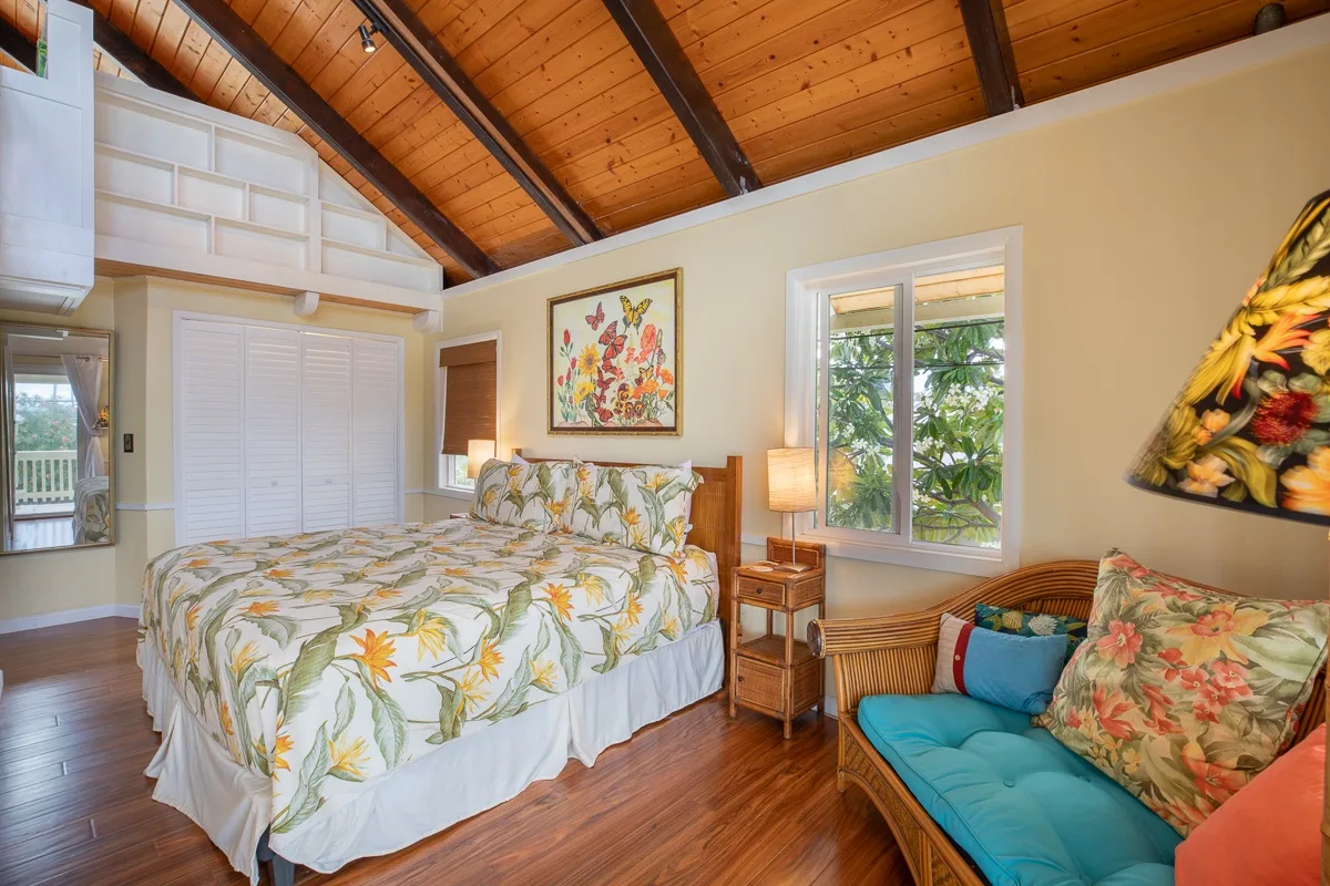 A bedroom with a bed and a cushioned seating area beneath a sloped wooden ceiling.
