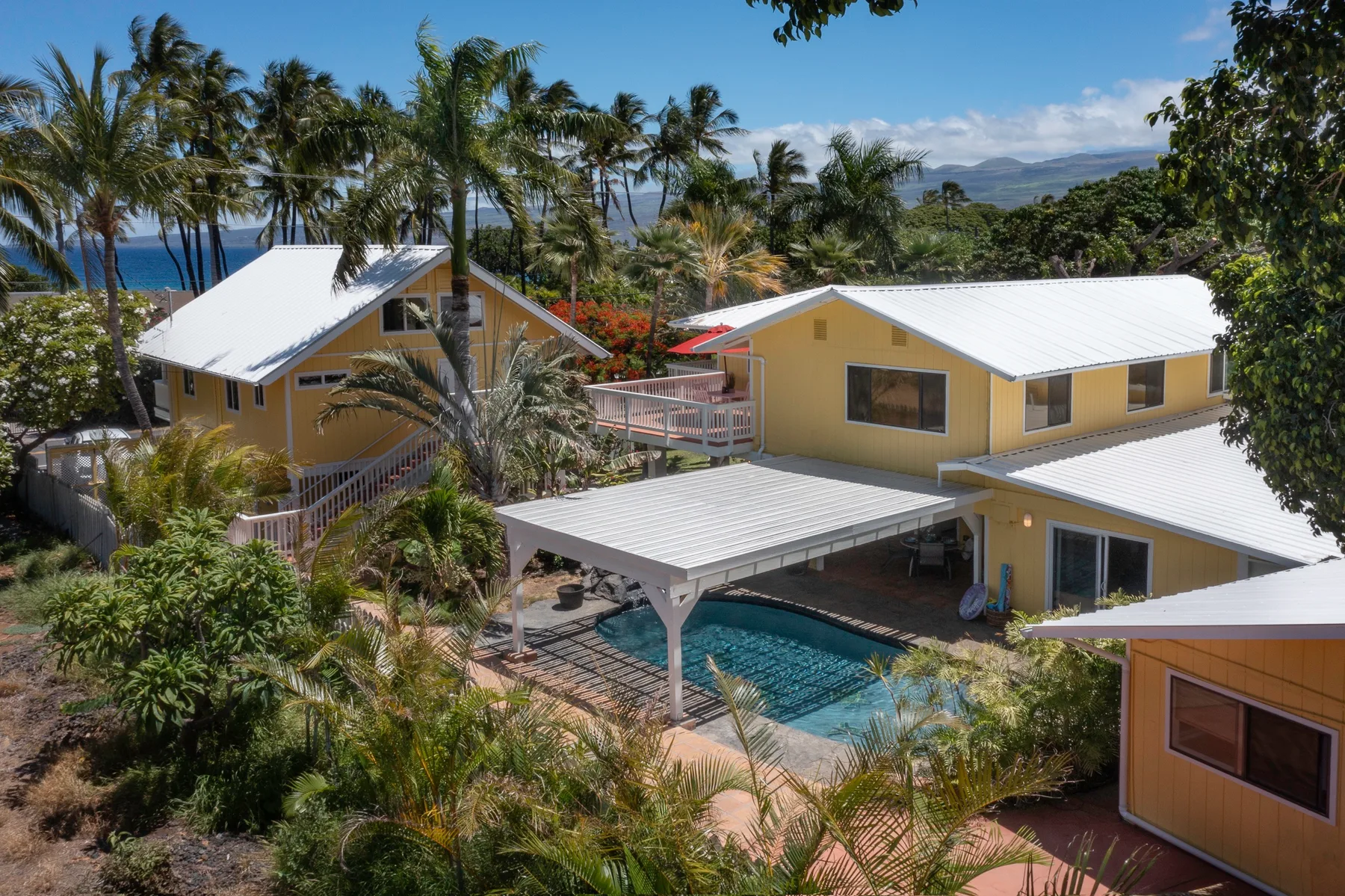 Aerial view of yellow buildings surrounding a swimming pool amid tropical greenery.
