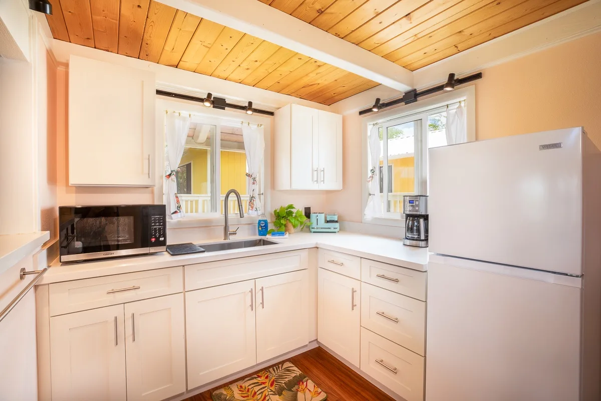 A bright kitchen with white cabinets, a sink, and a refrigerator.