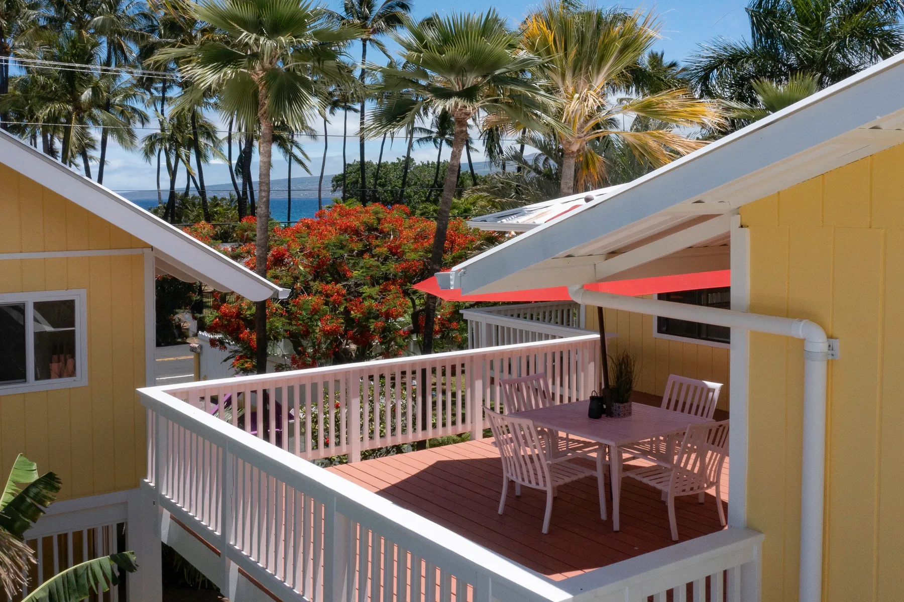 A raised deck with outdoor seating overlooks tropical trees and the ocean.