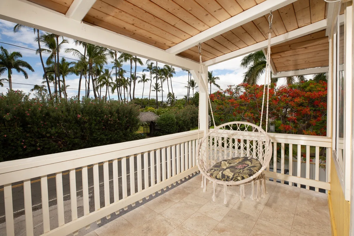 A covered outdoor porch with a hanging seat and views of tropical greenery.