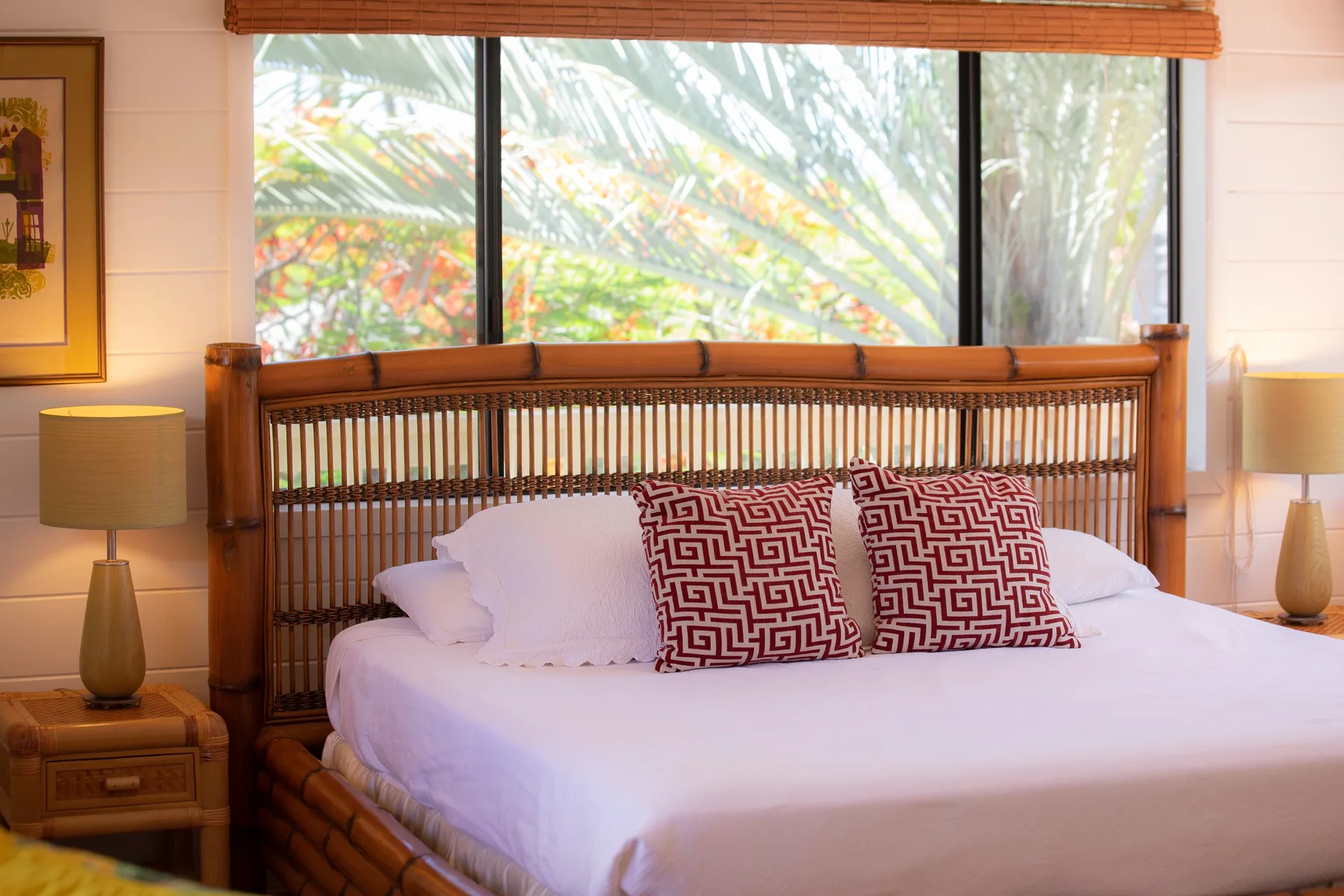 A bedroom with a bed, patterned pillows, and a large window overlooking greenery.