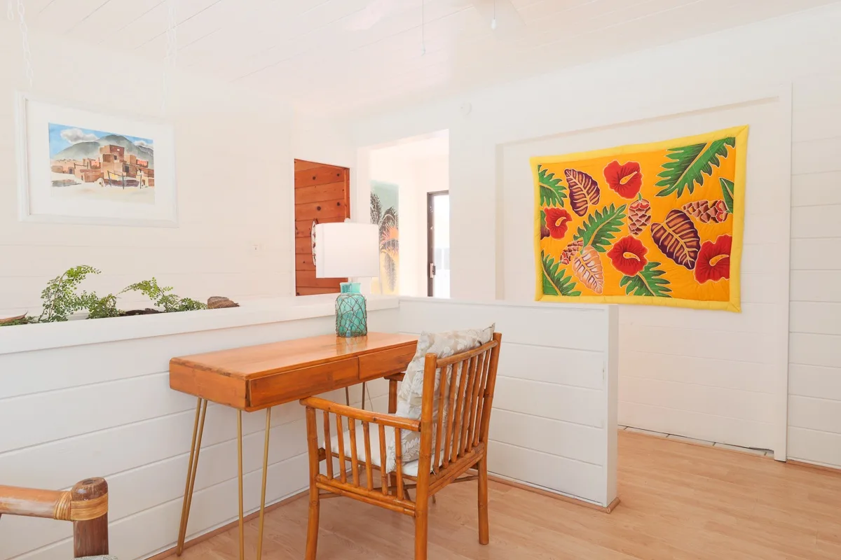 A bright room with a wooden desk, a chair, and a colorful floral wall hanging.