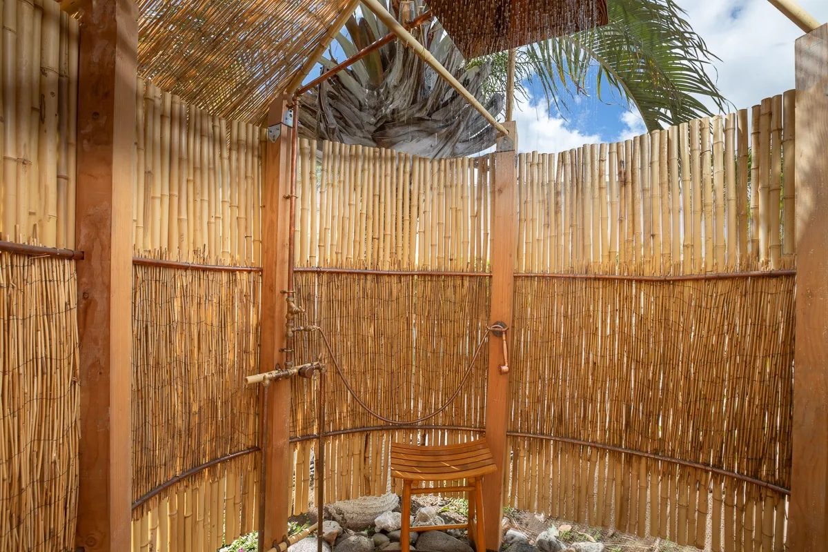 An outdoor shower area enclosed by bamboo fencing, with a wooden stool.