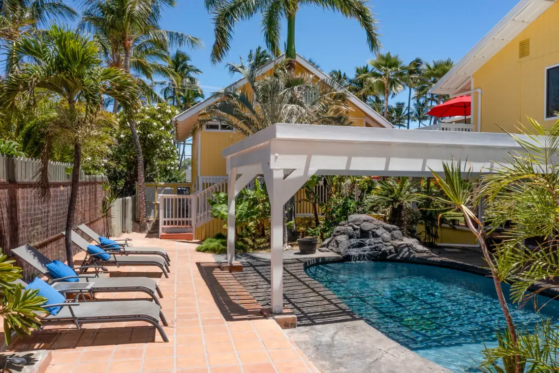 A sunny outdoor pool area with lounge seating and a shaded pergola.