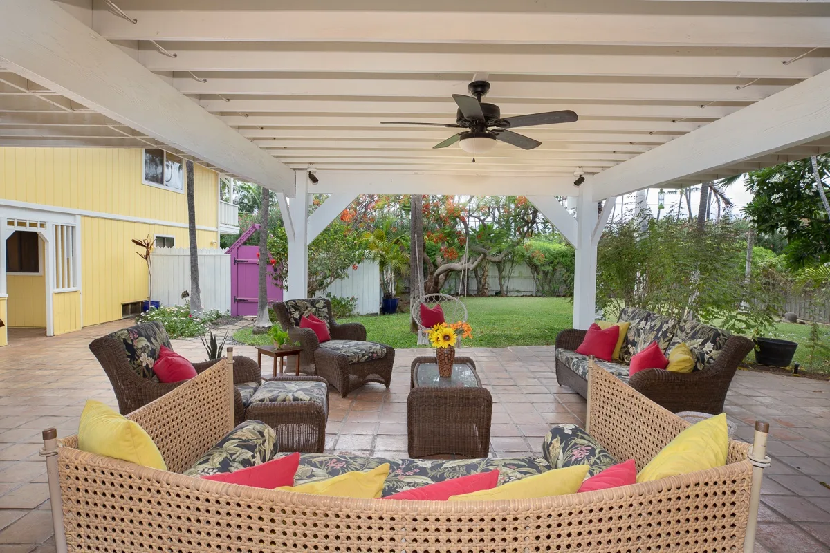 A covered outdoor patio with cushioned seating overlooks a green garden.