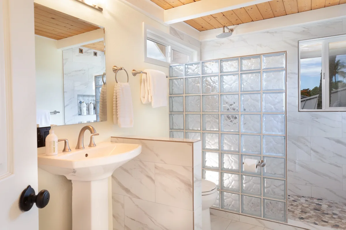 A bright bathroom with a pedestal sink and glass-block shower partition.
