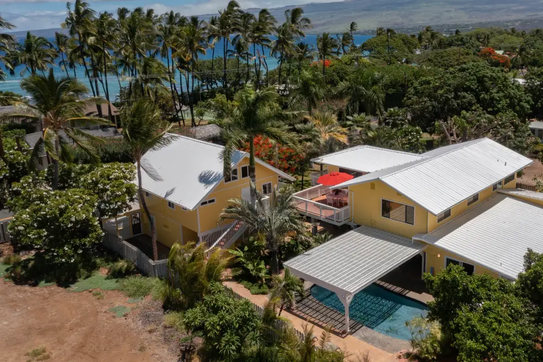 Aerial view of yellow buildings among tropical greenery, with a pool and coastline nearby.