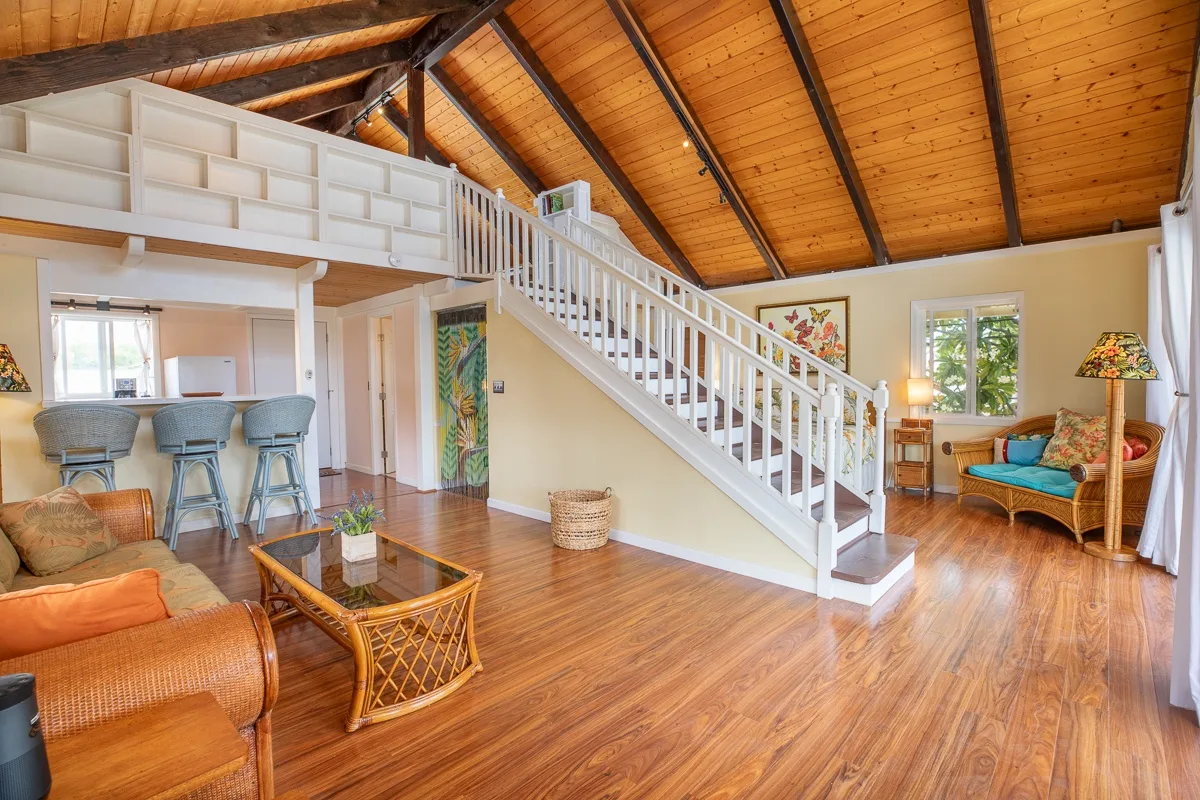 An open living room with a staircase, dining area, and seating beneath a wood-paneled ceiling.