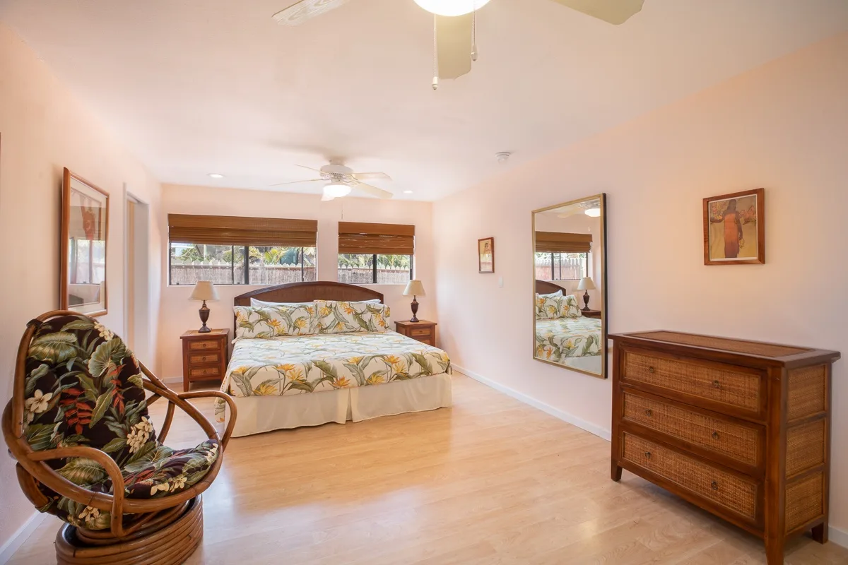 A bright bedroom with a patterned bed, a woven armchair, and wooden furnishings.