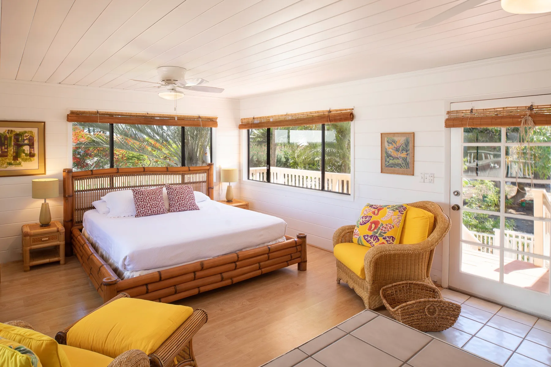 A bright bedroom with a wooden bed and a yellow armchair beside large windows.