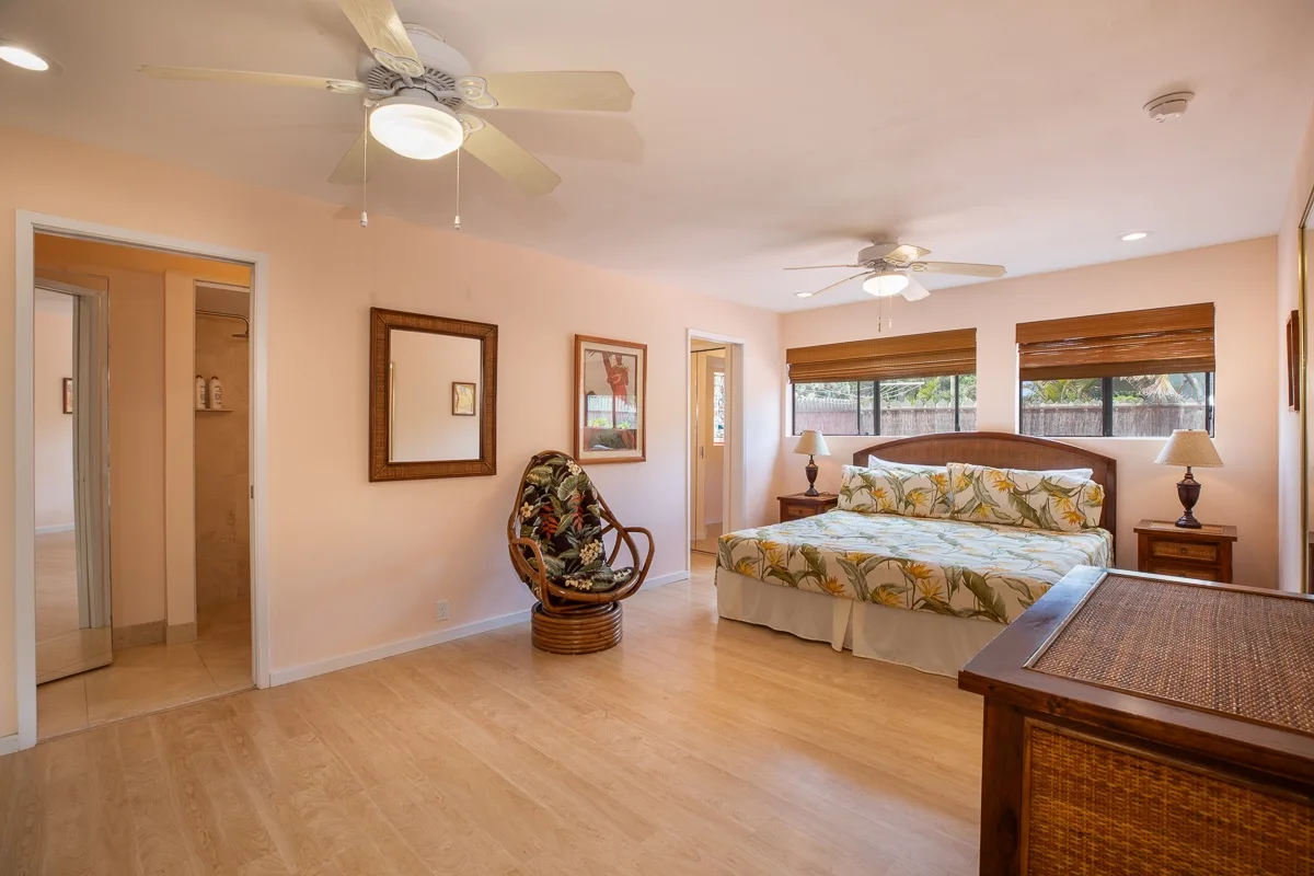A bedroom with a bed, ceiling fans, and windows with wooden blinds.