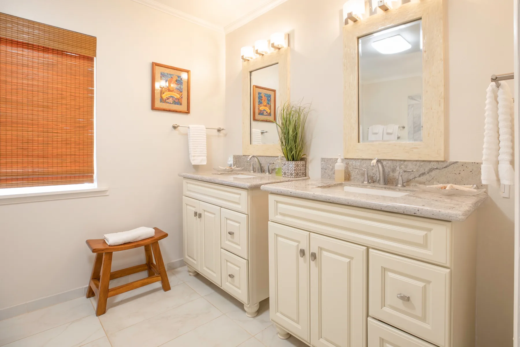 A bright bathroom with two vanities, mirrors, and a window with a bamboo shade.