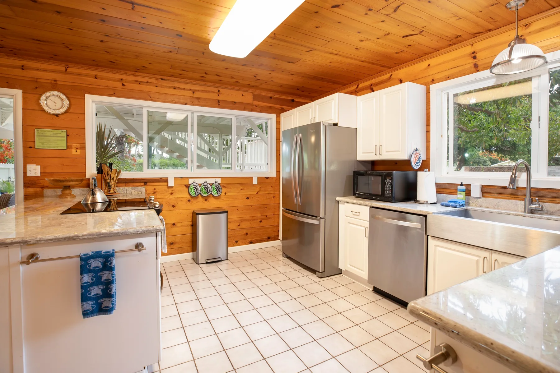 A bright kitchen with wooden walls, white cabinets, and stainless steel appliances.