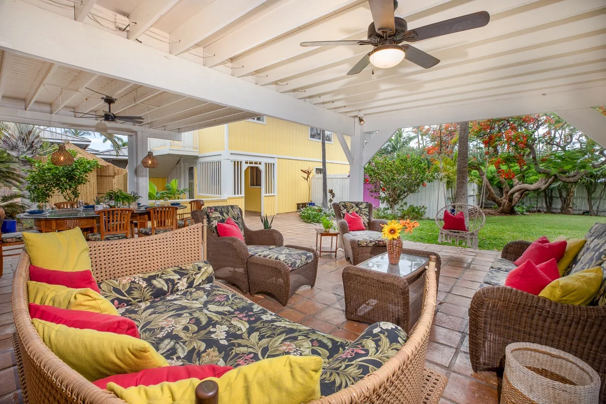 A covered patio with wicker seating opens onto a leafy garden.