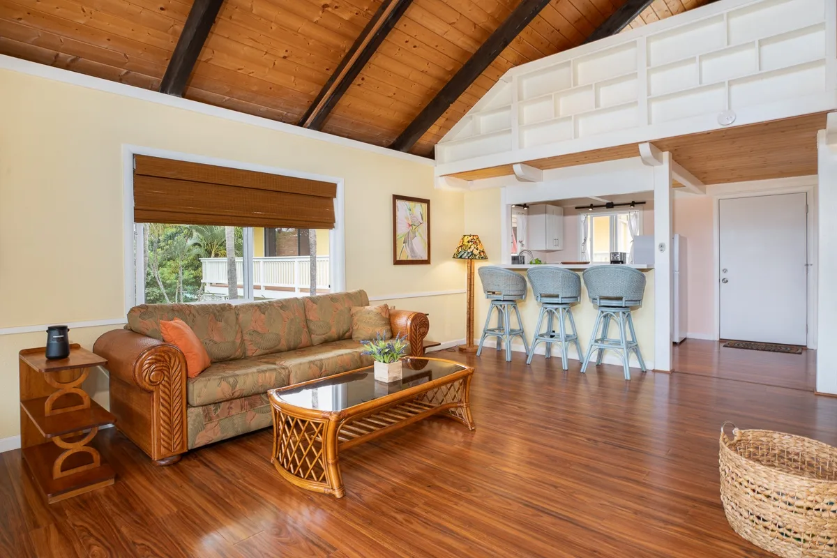 A living room with a sofa, coffee table, and kitchen counter with stools.