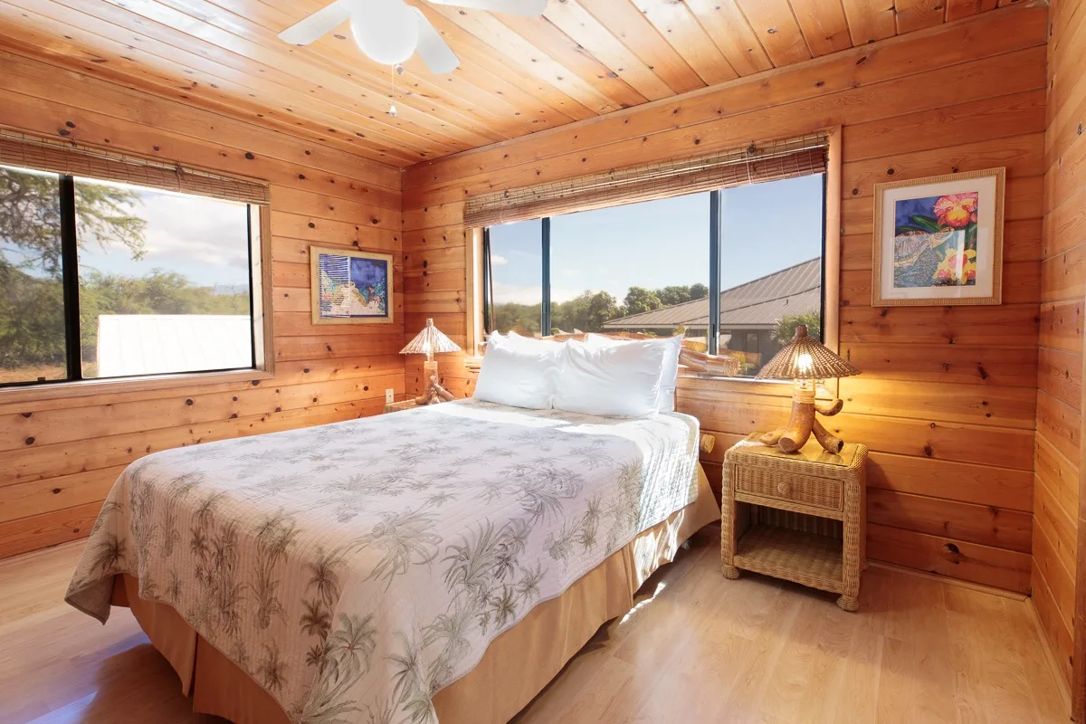 A bedroom with a bed beneath large windows in a wood-paneled room.