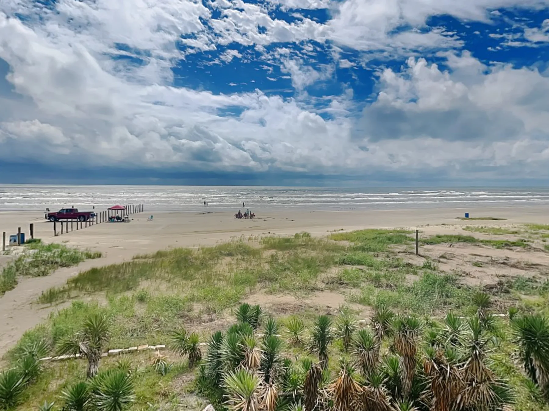 Una playa de arena se extiende hacia el océano bajo un cielo azul y nublado.