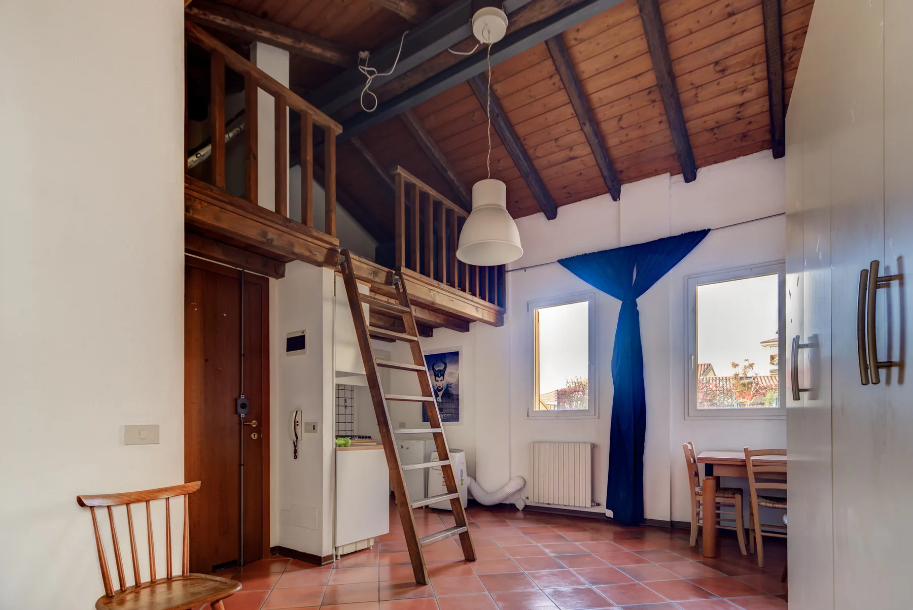 Una habitación con una zona elevada de madera para dormir, una escalera y una mesa de comedor.