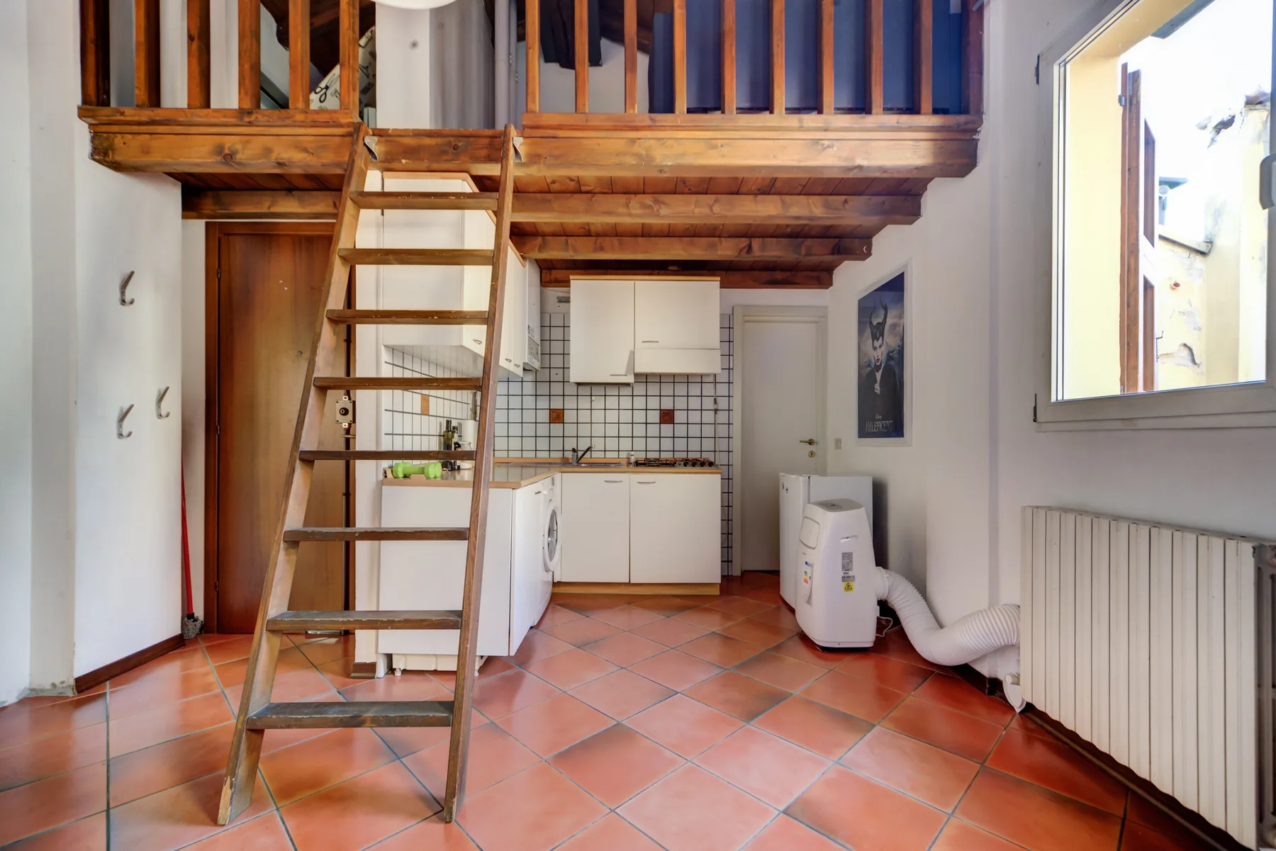 Una cocina compacta está bajo un altillo de madera, con una escalera que sube.