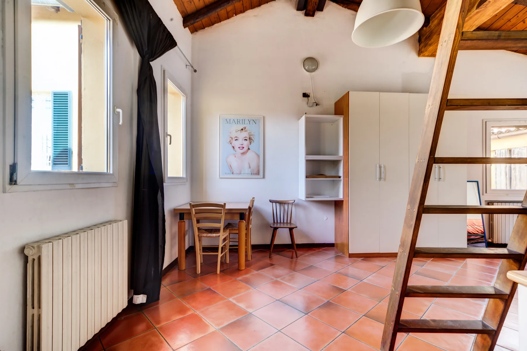 Una pequeña habitación abuhardillada con mesa, sillas y armarios.