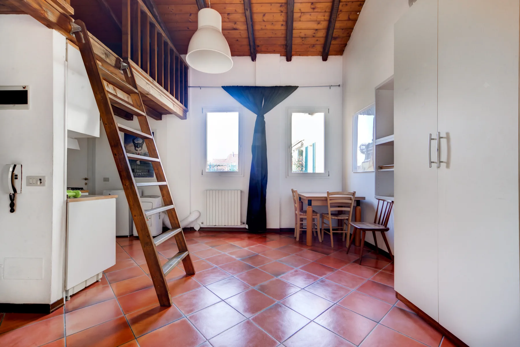 Un comedor con una mesa y sillas de madera junto a una escalera de altillo.
