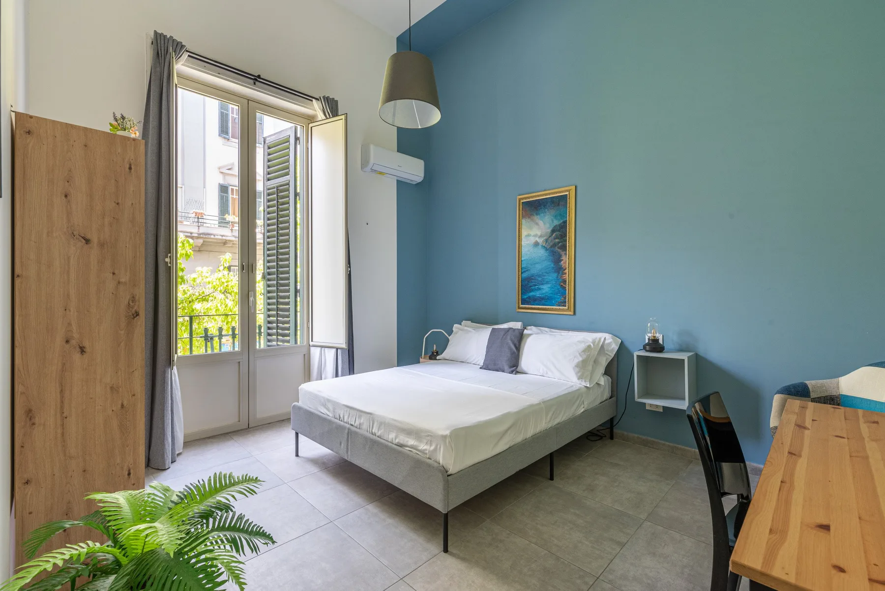 Un dormitorio con cama, pared azul y puertas abiertas al balcón.