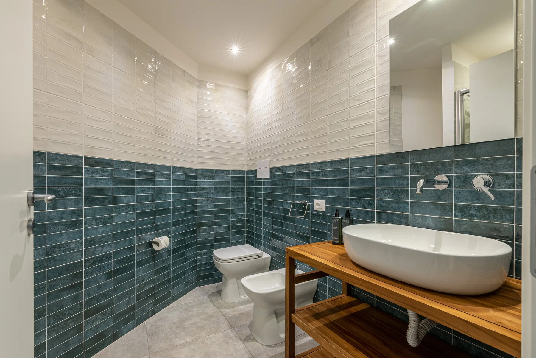 A tiled bathroom with a toilet and a basin on a wooden vanity.