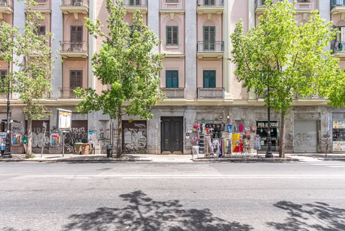 Street scene with storefronts beneath a residential building and trees along the sidewalk.