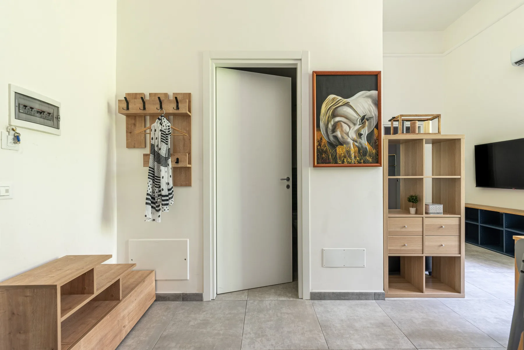 A bright interior entryway with a doorway, wall hooks, and open shelving.