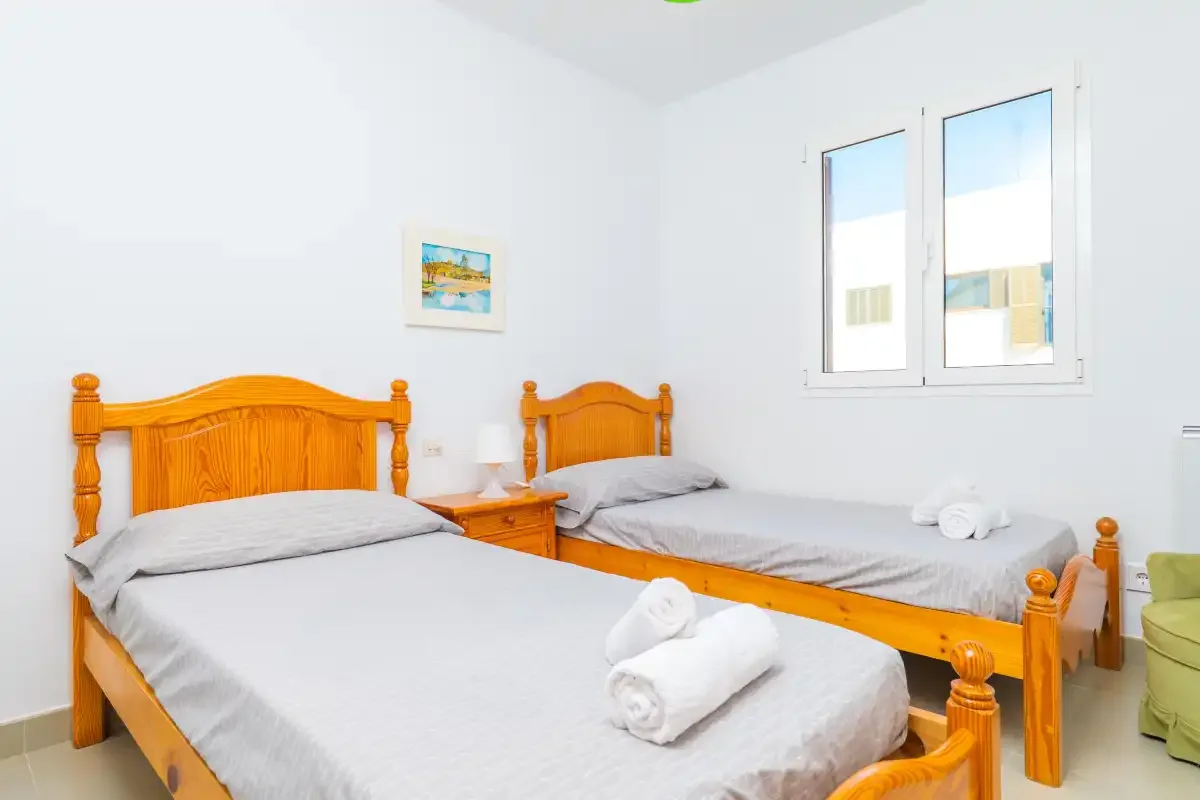A bright bedroom with two wooden beds and folded towels.