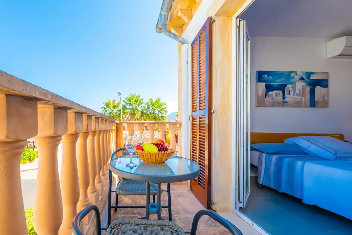 A balcony with a round table overlooks palm trees, beside an open bedroom.