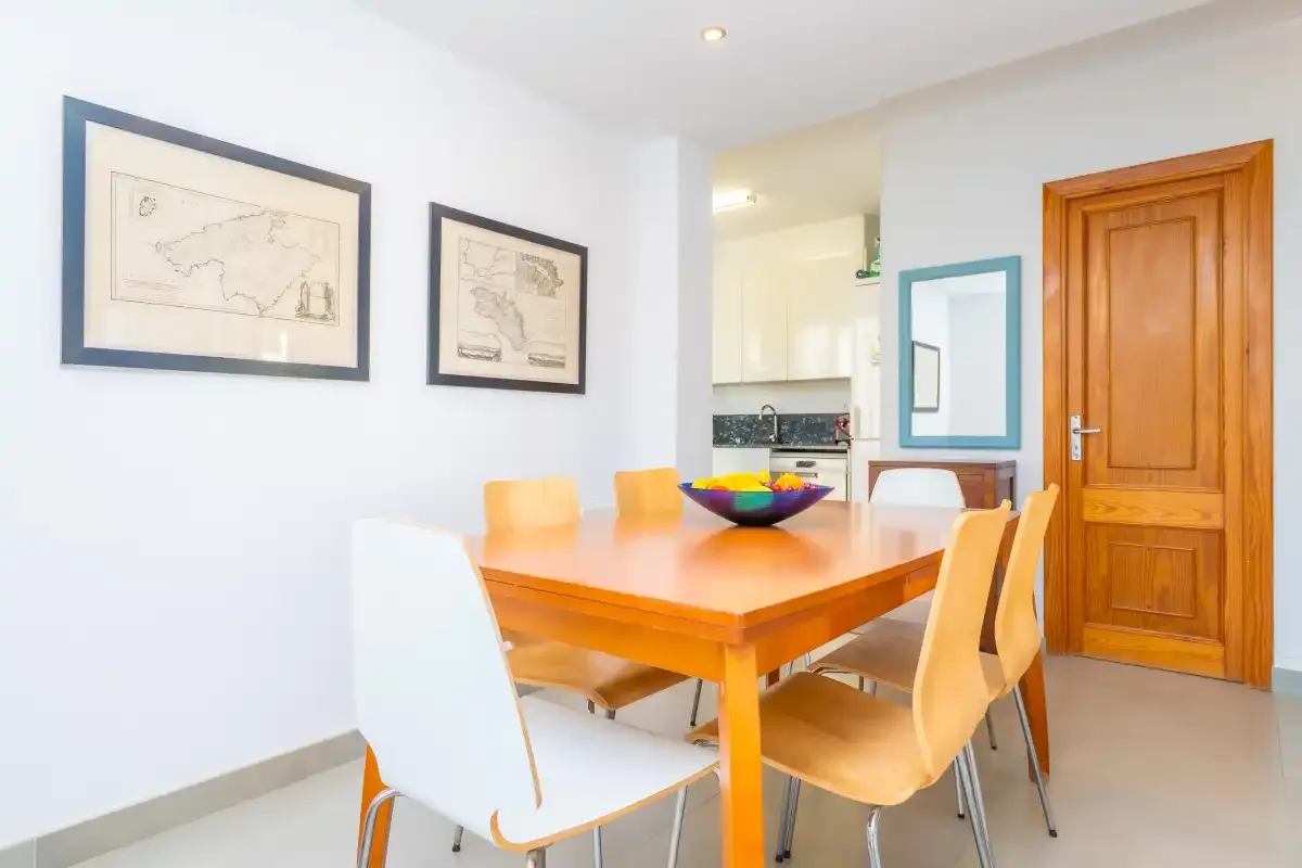 A dining area with an orange table and chairs beside a small kitchen.