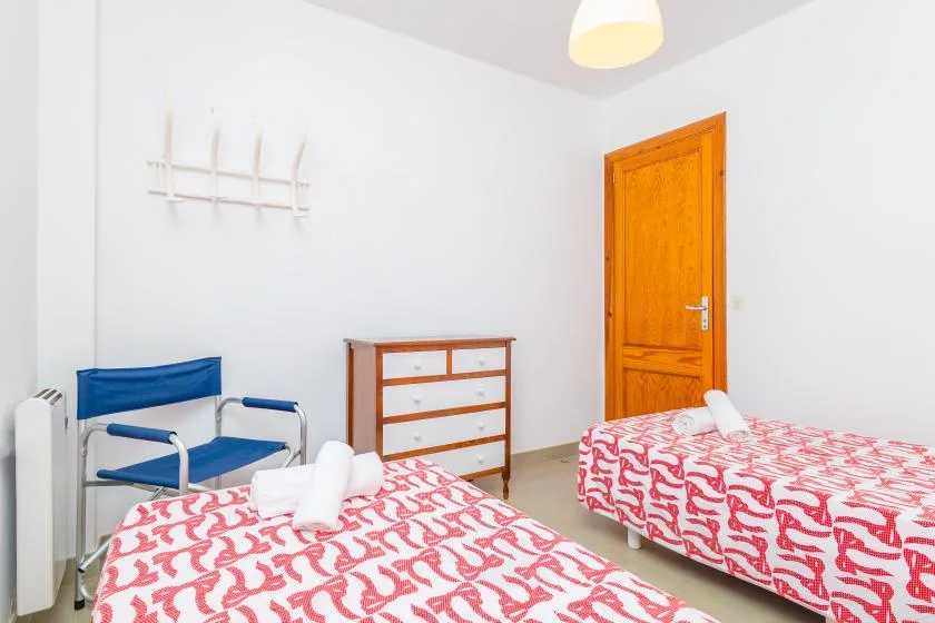 A bedroom with two beds, a small dresser, and a blue chair.