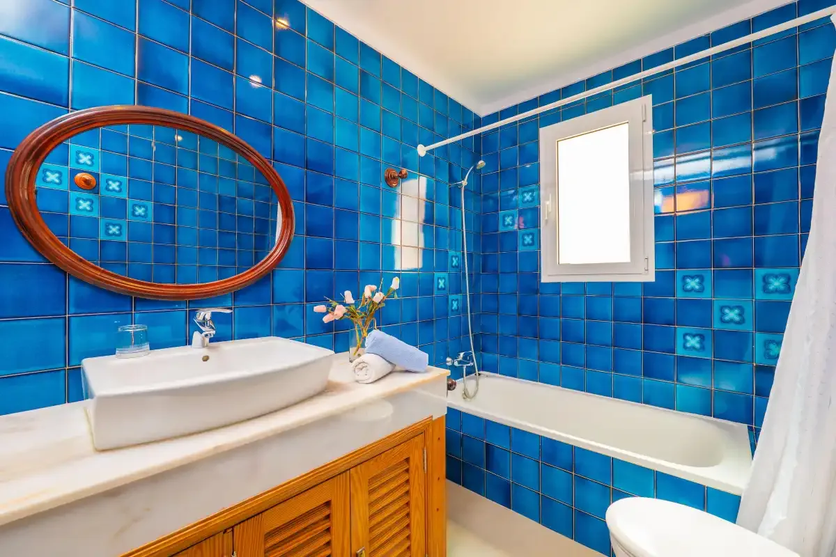 A bathroom with a white bathtub, basin, and vivid blue tiled walls.