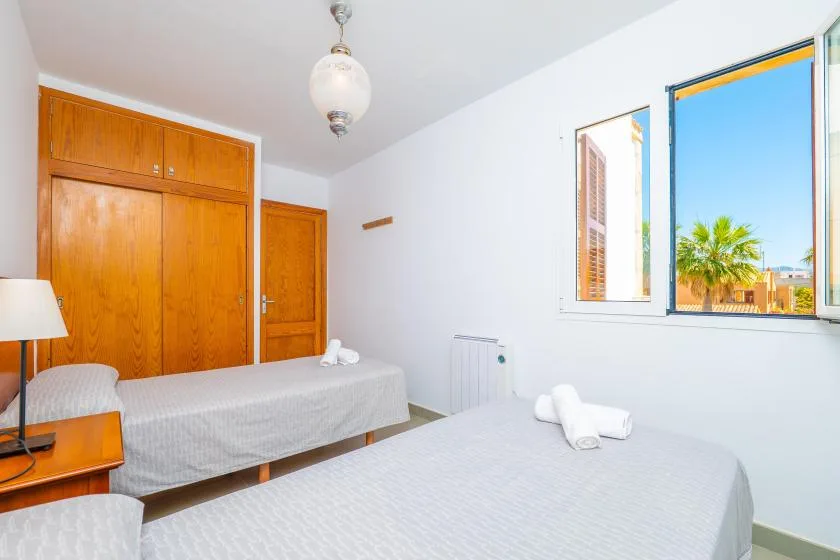 A bright bedroom with two beds beside an open window.
